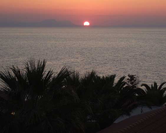 Крит. Вечерний вид с балкона.
      Солнце опускается за гору в море.